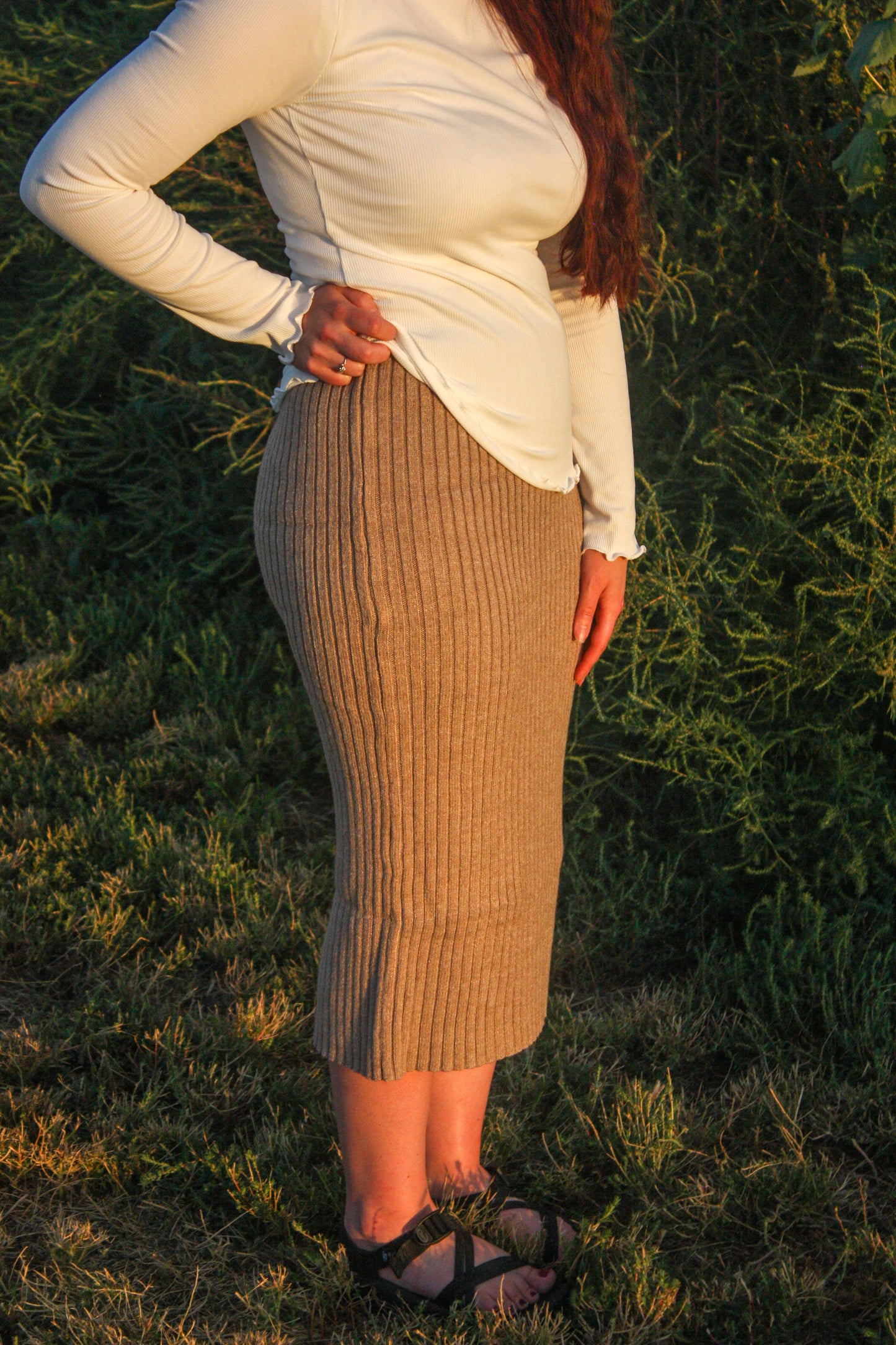 Person wearing a white top and brown ribbed skirt standing in a natural setting.