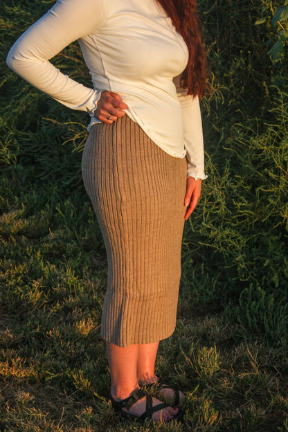 Person wearing a white top and brown ribbed skirt standing in a natural setting.