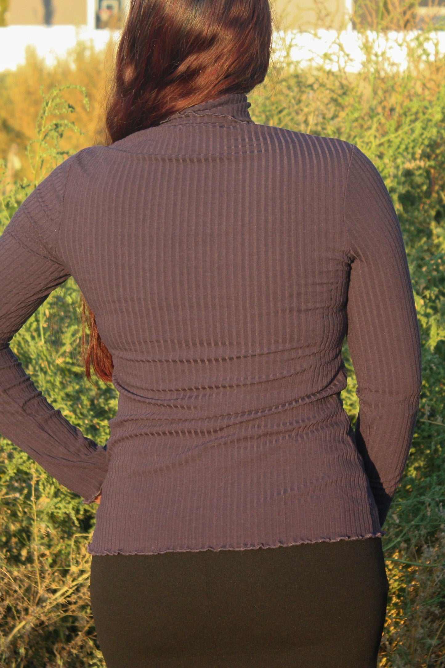 Woman wearing a navy ribbed mock neck, long-sleeve top with lettuce hem detailing and black skirt standing in a natural setting.