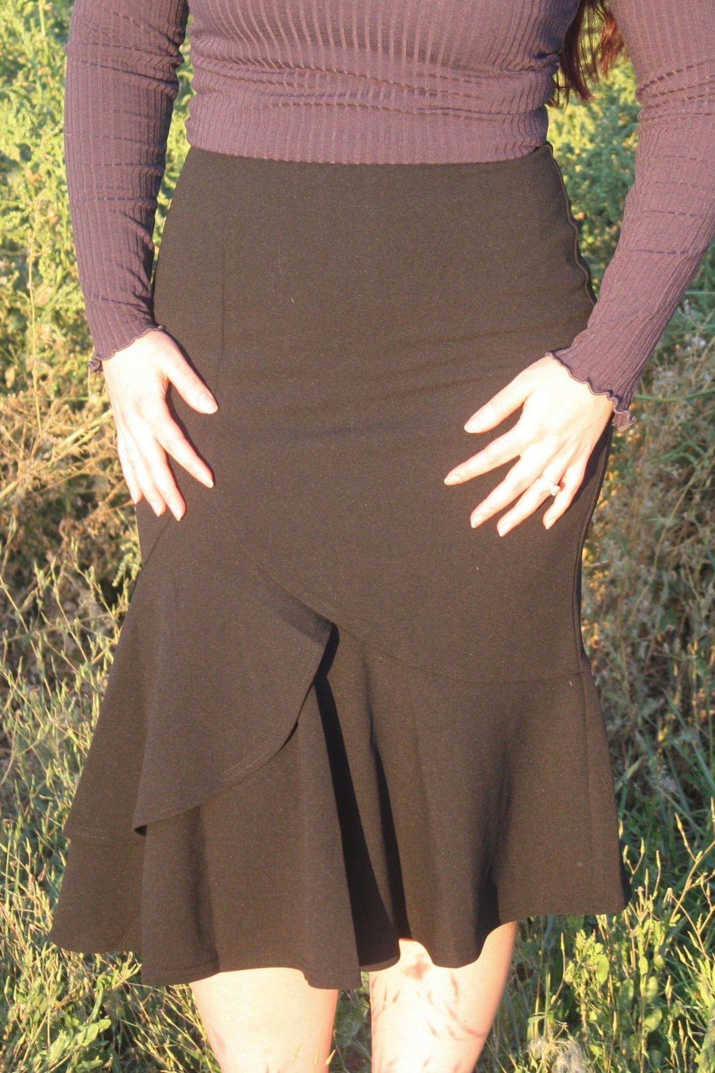 Person wearing a navy ribbed long sleeve top and black midi skirt with a ruffle mermaid style bottom standing in a grassy outdoor setting