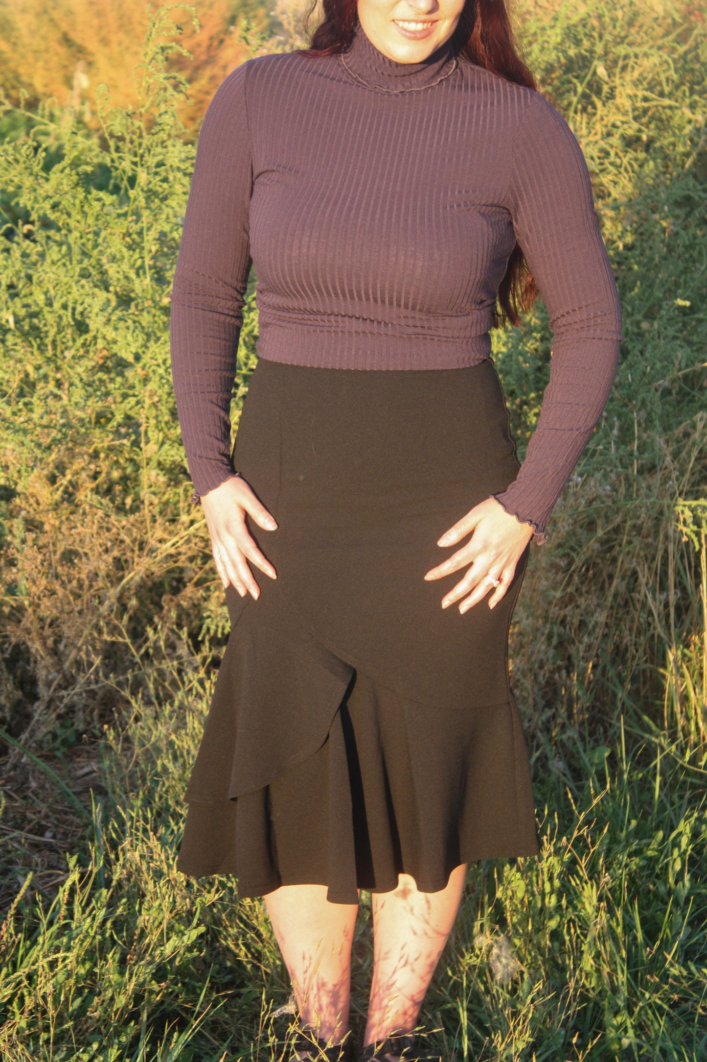 Person wearing a navy ribbed long sleeve top and black midi skirt with a ruffle mermaid style bottom standing in a grassy outdoor setting