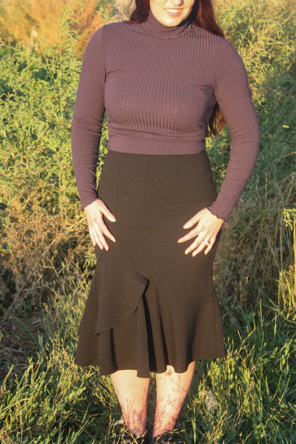 Person wearing a navy ribbed long sleeve top and black midi skirt with a ruffle mermaid style bottom standing in a grassy outdoor setting