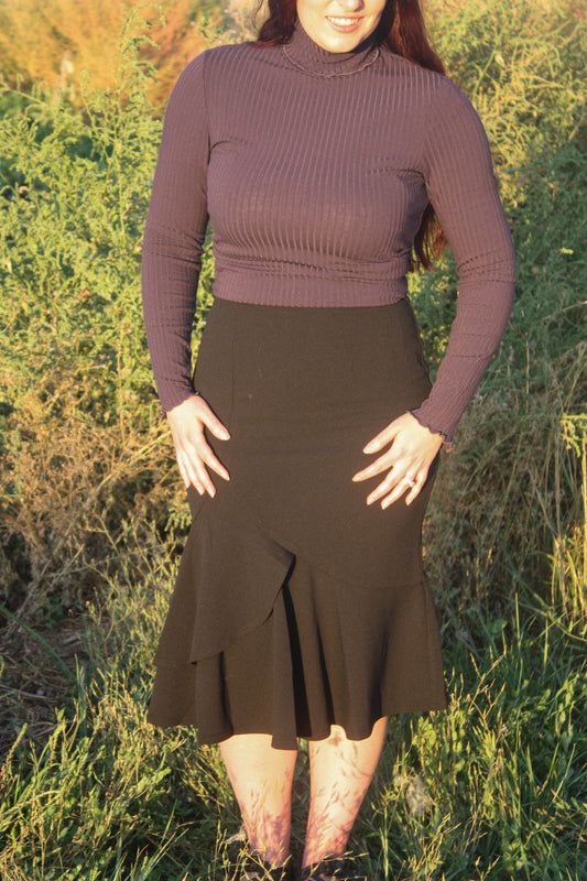 Person wearing a navy ribbed long sleeve top and black midi skirt with a ruffle mermaid style bottom standing in a grassy outdoor setting