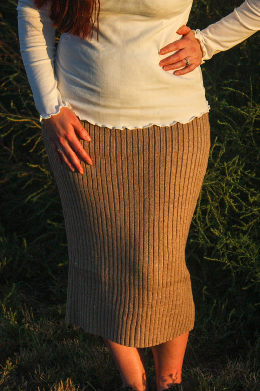Person wearing a beige ribbed form fitting midi skirt and white long-sleeve top standing in a natural setting.