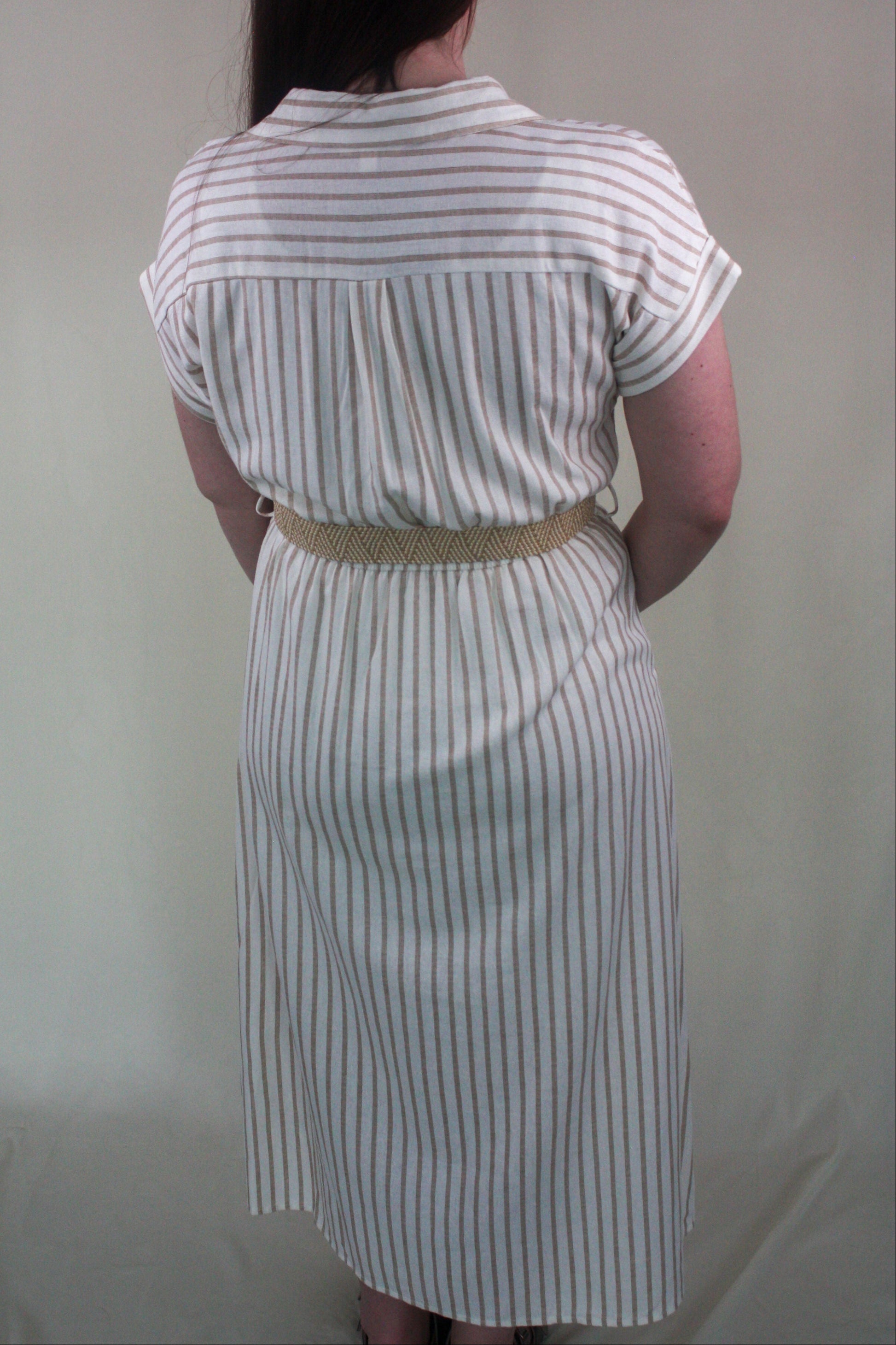 Person wearing a white and khaki striped dress with a belt against a plain background